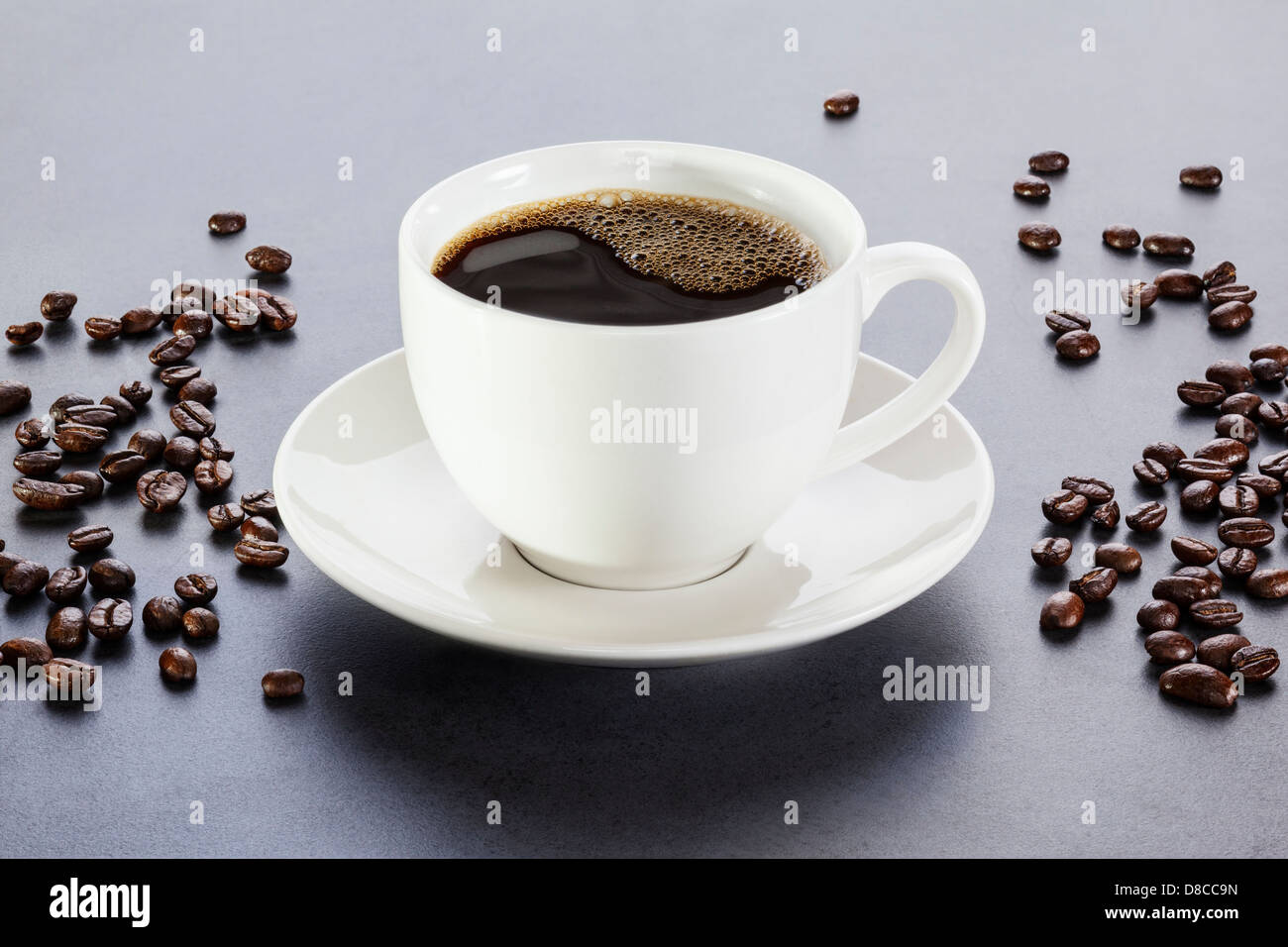 Kaffee - Tasse Espresso oder Kaffee auf einem grauen Hintergrund mit Kaffeebohnen verstreut. Von vorne nach hinten Fokus. Stockfoto