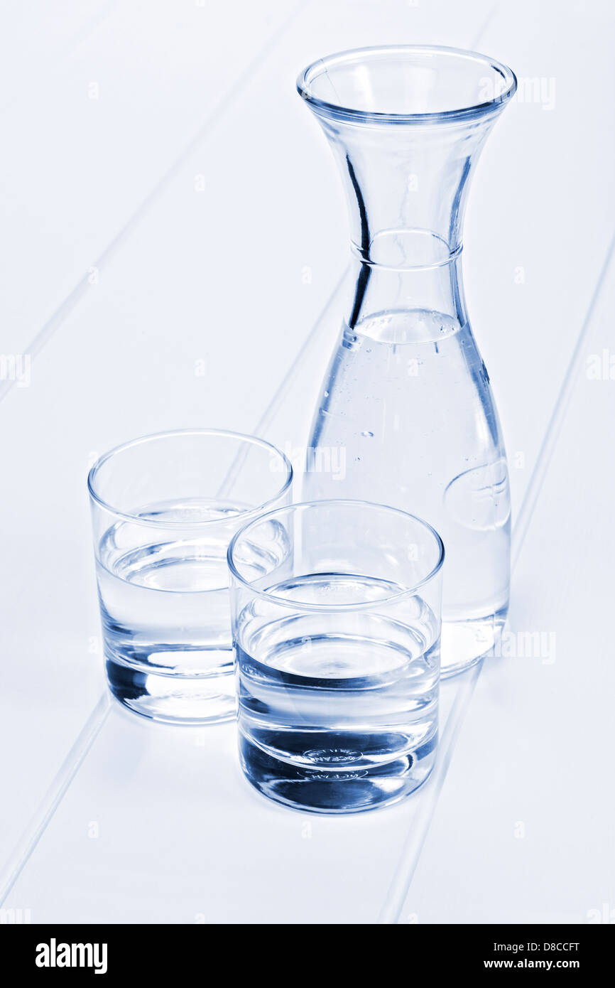 Wasserkaraffe und zwei Gläser - eine Karaffe Wasser auf einem Tisch mit zwei Gläsern, blau getönt. Stockfoto