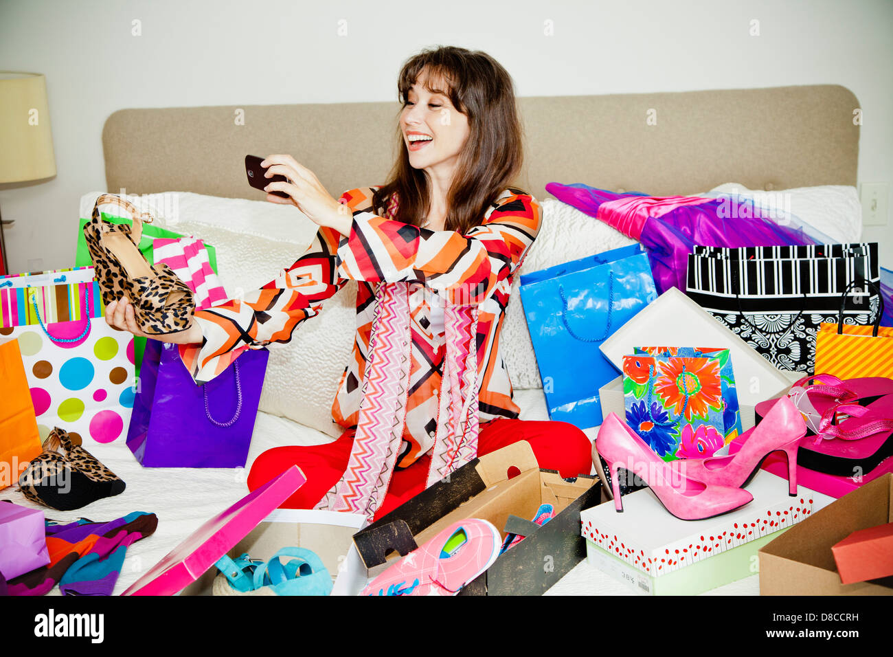 Frau auf Bett umgeben von Einkaufstaschen Stockfoto