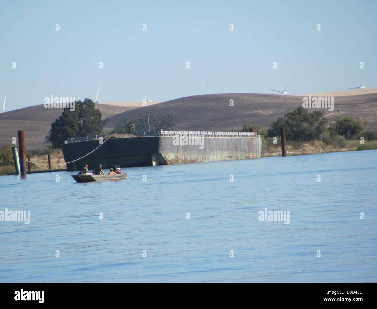 Eine Gruppe von Personen befindet sich in einem kleinen Boot neben einem großen Transportboot. Das Foto zeigt den Größenkontrast zwischen den beiden Schiffen, wobei das kleinere Boot im Vordergrund und das größere im Hintergrund steht. Stockfoto