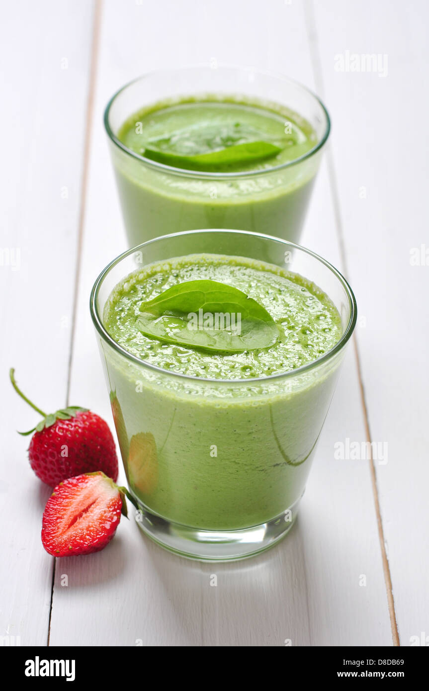 Spinat-Smoothies im Glas serviert mit Erdbeeren auf einem hölzernen Hintergrund Stockfoto