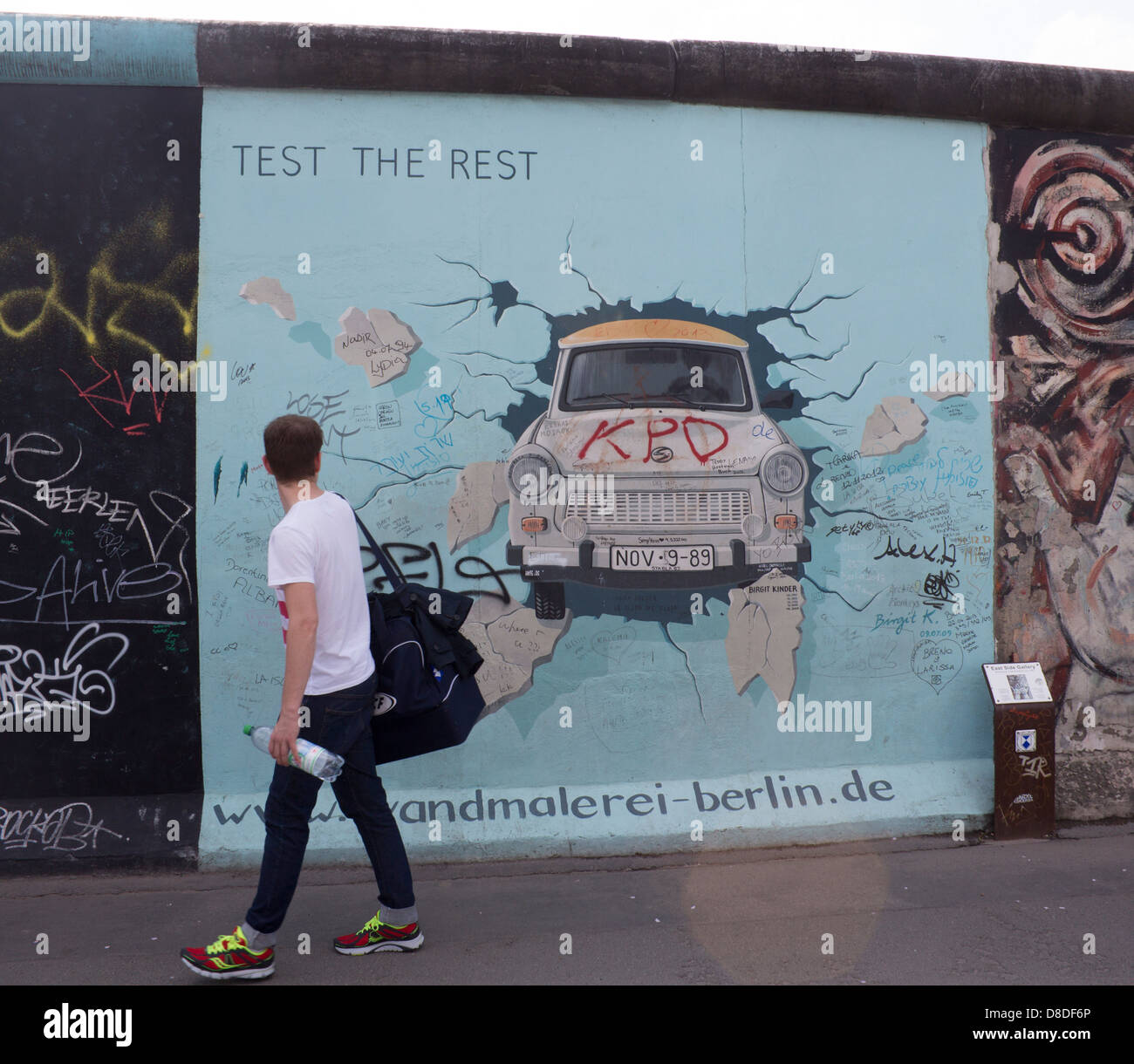 East Side Gallery Berlin Wandmalerei des Trabant Auto Wand durchbrechen, mit dem Menschen vorbeigehen, rückblickend Berlin Deutschland Stockfoto