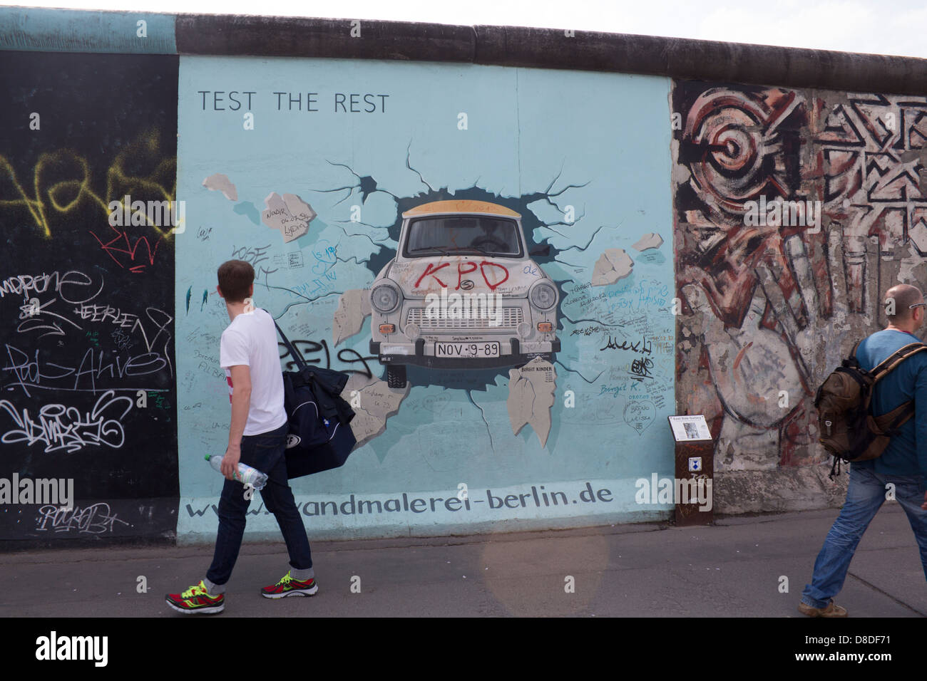East Side Gallery Berlin Wandmalerei des Trabant Auto Wand durchbrechen, mit dem Menschen vorbeigehen, rückblickend Berlin Deutschland Stockfoto