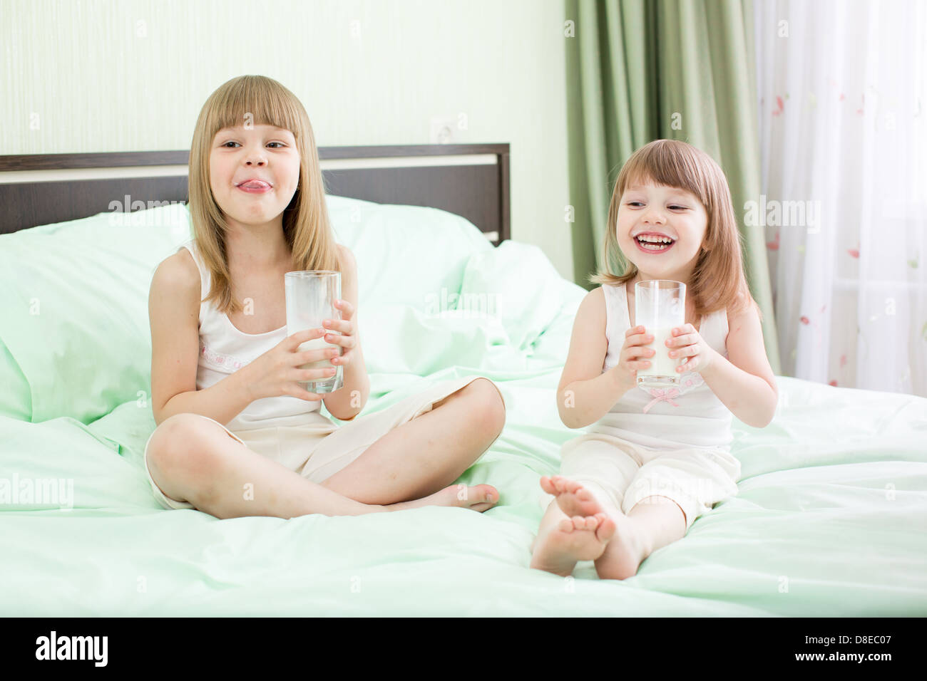 Zwei kleine Mädchen trinken Milch auf Bett Stockfoto