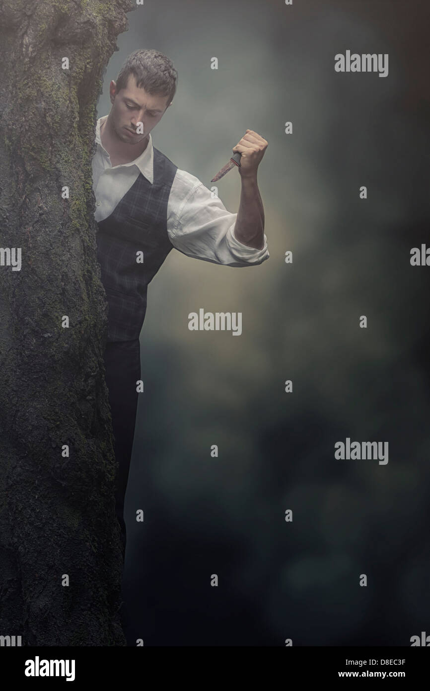ein Mann mit einem Messer hinter einem Baum versteckt Stockfoto