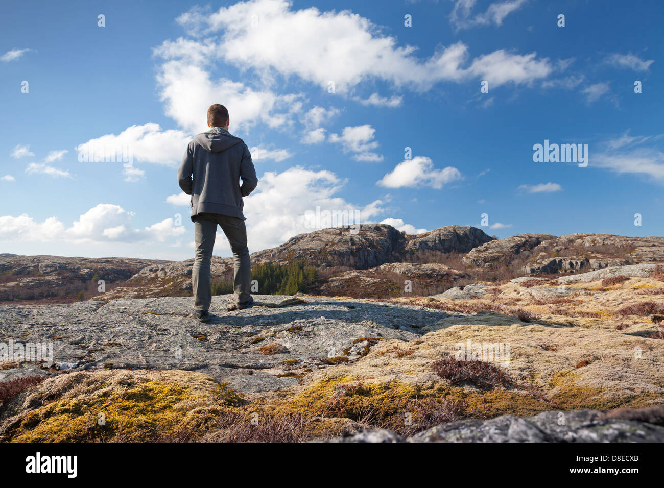 Junger Mann auf dem Felsen steht und schaut über den Horizont Stockfoto