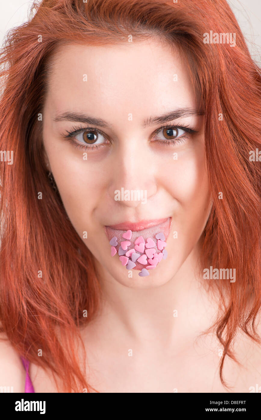 Lustige romantische Porträt Frau mit roten Haaren, die Zunge klebt bedeckt Zuckerherz Stockfoto