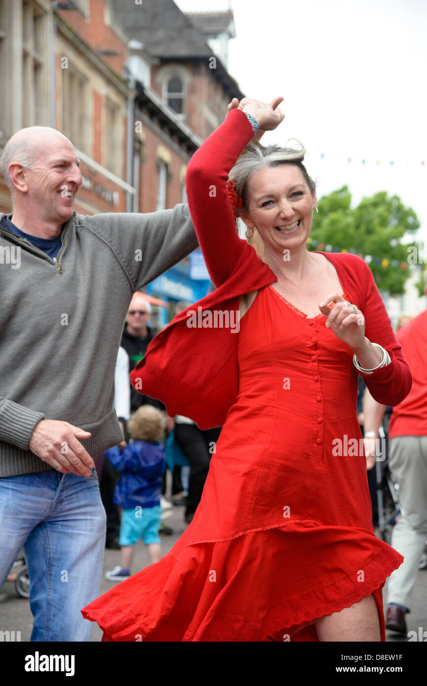 Glücklich lachende Frau trägt ein rotes Kleid tanzen in den Straßen, UK. Paare tanzen zusammen. Stockfoto