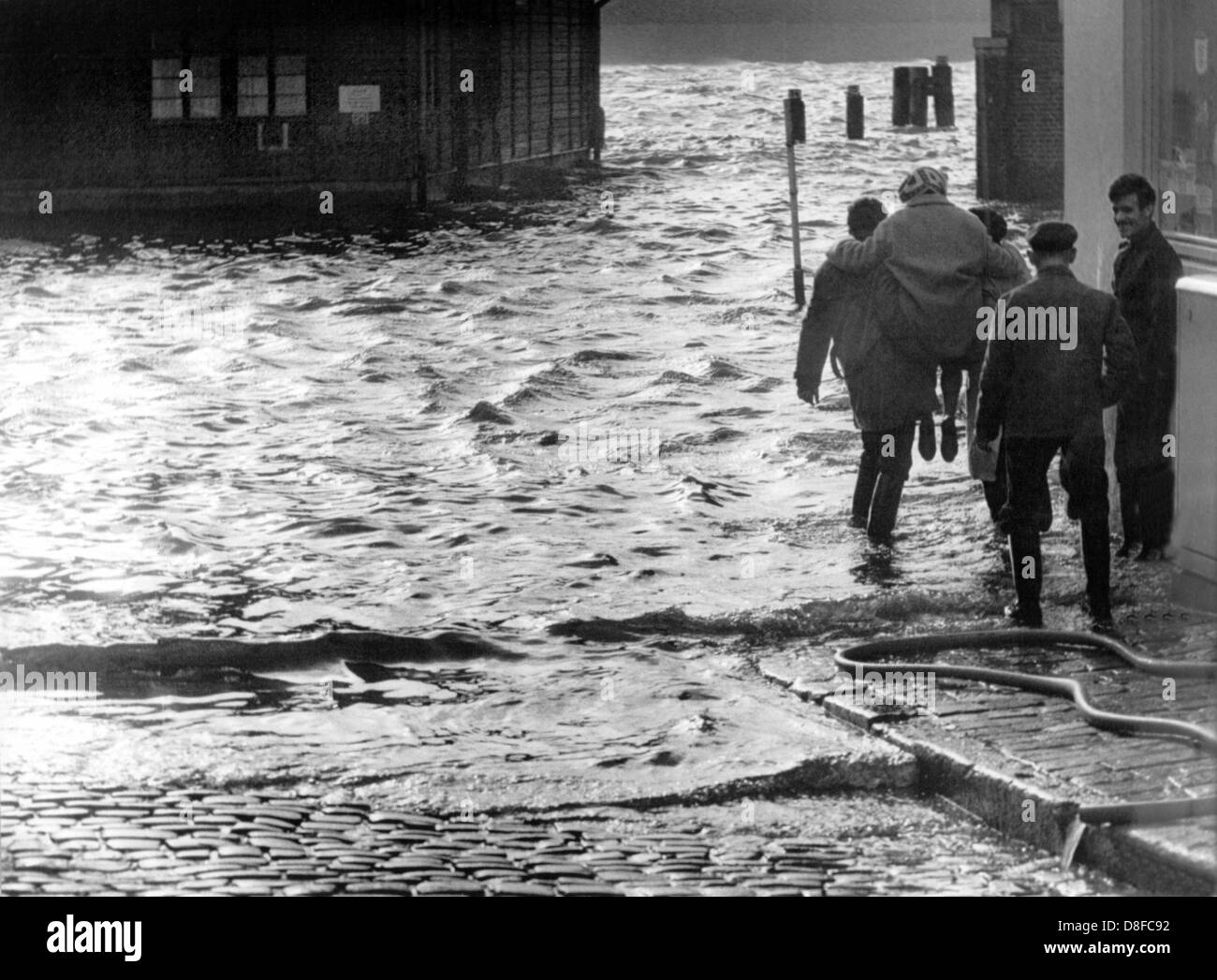 Zwei Männer tragen eine Frau über die überfluteten Fischmarkt in Hamburg am 2. November 1965. Die prognostizierten Sturmflut hatte Norddeutschland genauso ernst nehmen wie befürchtet nicht beschädigt. Stockfoto