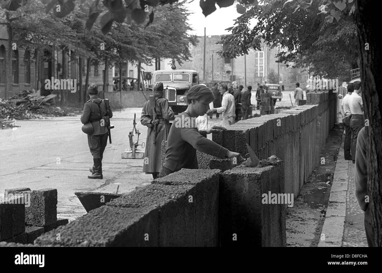 Bauarbeiter der Ost-Berliner reichen von "Potsdamer Platz" Platz in Richtung der "Lindenstraße" Straße unter der Aufsicht von bewaffneten Offizieren der Volkspolizei in Berlin, DDR, 18. August 1961 die Berliner Mauer. Die Mauer ist zwischen zwei und fünf Metern innerhalb der Demarkationslinie der Sektoren in Ost-Berlin. Hier verlaufen die Grenzen der Sektoren auf die Hausfassaden. Grit Betonplatten und hohle Ziegelsteine, die zunächst für den Bau von Häusern in Ost-Berlin konzipiert wurden, werden für den Bau verwendet. Die Bauarbeiter sind 1,28 DM pro Stunde bezahlt. In Stockfoto