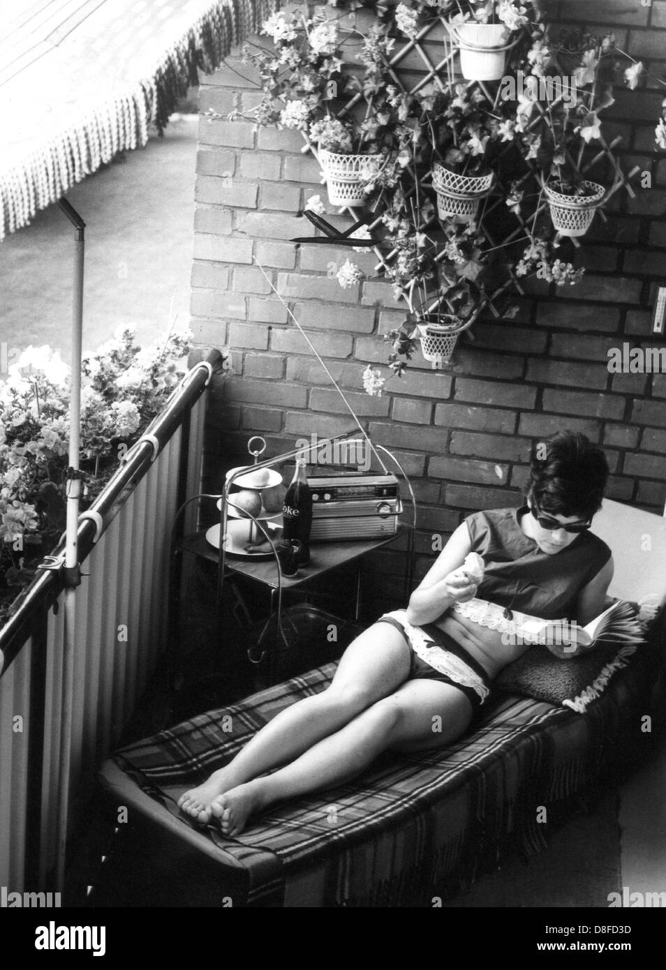 Liegestuhl, Sonnenschirm, Radio, Lektüre und ein kühles Getränk: eine junge Frau verbringt ihren Urlaub auf ihrem Balkon fotografiert am 29. Juli 1968. Stockfoto