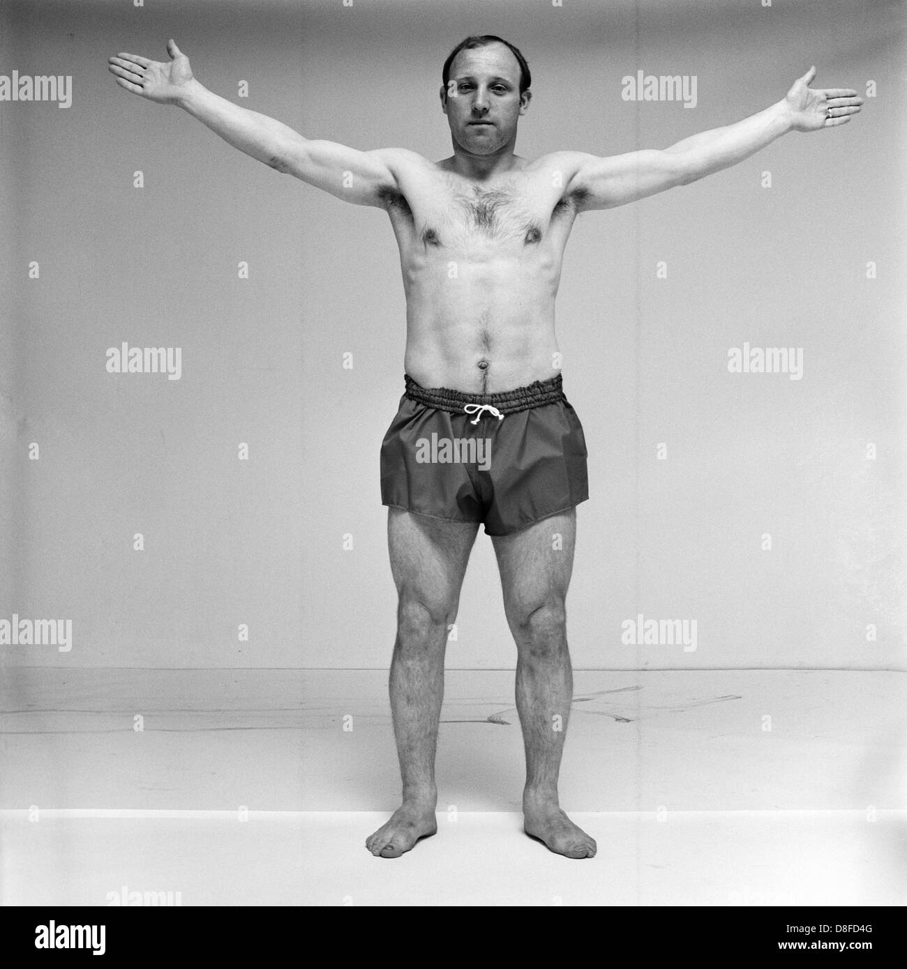 Fußballspieler Uwe Seeler trägt Shorts und breitet seine Arme in einem Fotostudio (schwarz-weiß-Fotografie). Stockfoto