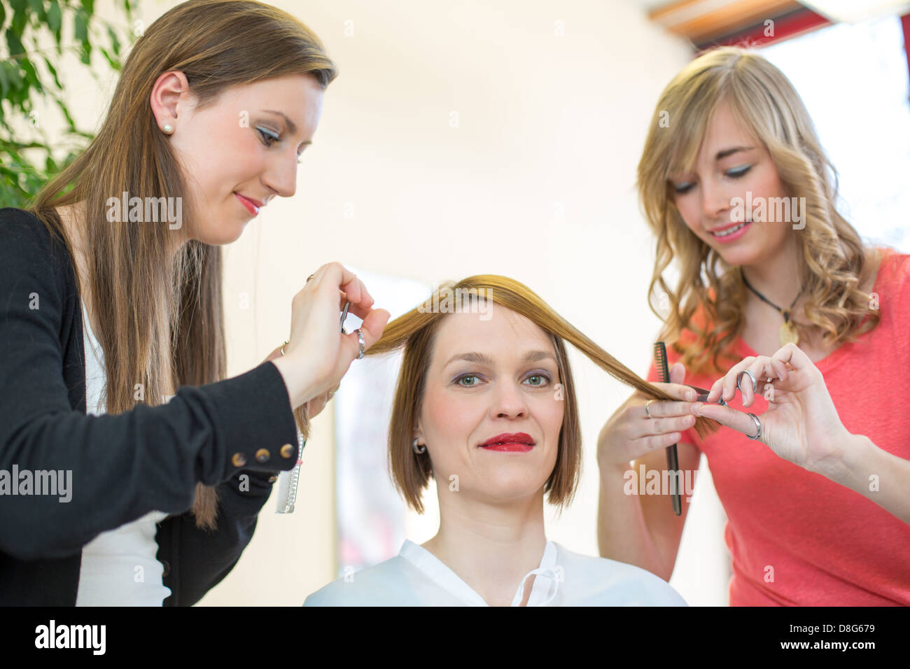 Zwei Friseure mit Kamm und Schere mit einem Kunden bei der Arbeit Stockfoto
