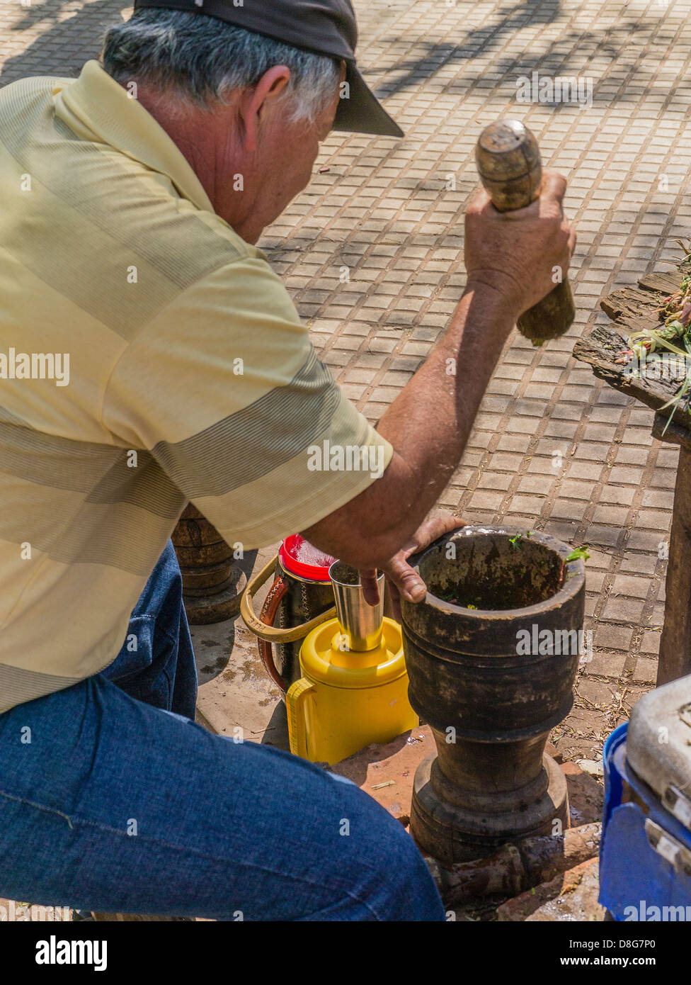 Ein Hispanic Mann sitzt auf dem Bürgersteig ein Stadtpark und Pfunde Yerba Mate Pflanzenblätter mit einem hölzernen Mörser und Stößel. Stockfoto