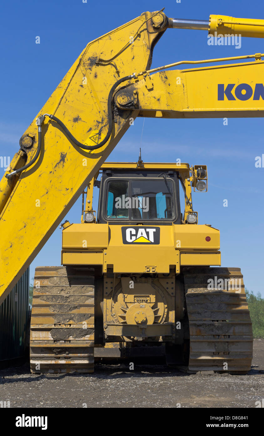 Gelbe Baggerarm mit gelben Traktor im Hintergrund gegen blauen Himmel Stockfoto