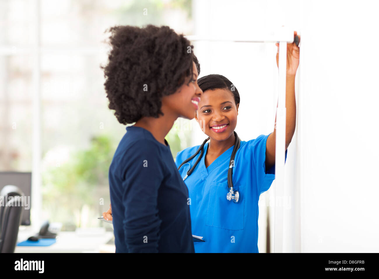 freundlichen afrikanischen Krankenschwester, die Messung der Höhe des Patienten Stockfoto