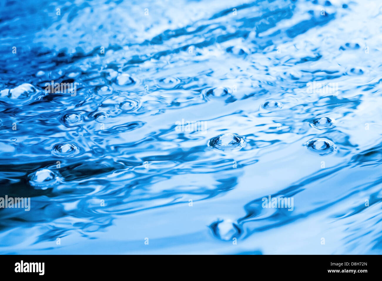 Hell leuchtende blaue Wasserfläche mit Welligkeit und Luftblasen Stockfoto