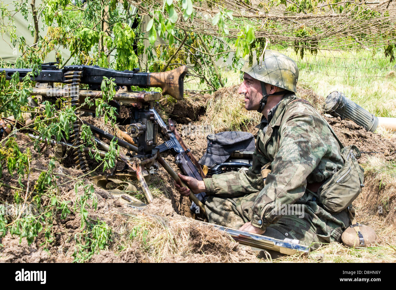 Overlord, d-Day-Re-Enactment Denmead 2013. Deutscher MG-Schütze in einem Graben hinter Tarnung versteckt. Stockfoto