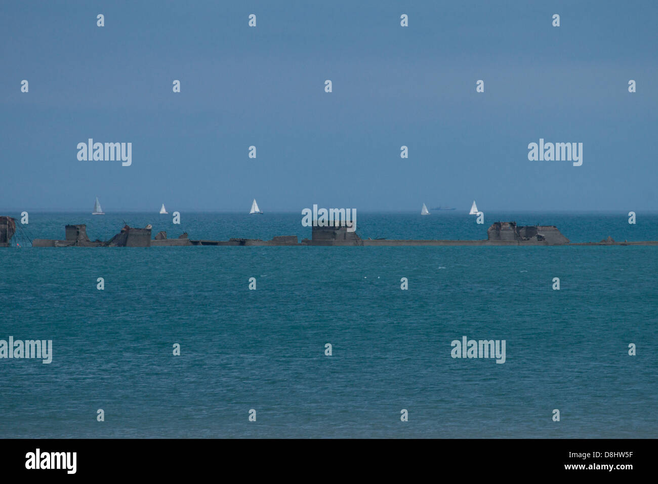 Arromanches, Normandie, Frankreich. Reste der "Mulberry" künstliche Hafen mit Booten im Hintergrund aus dem zweiten Weltkrieg. Stockfoto