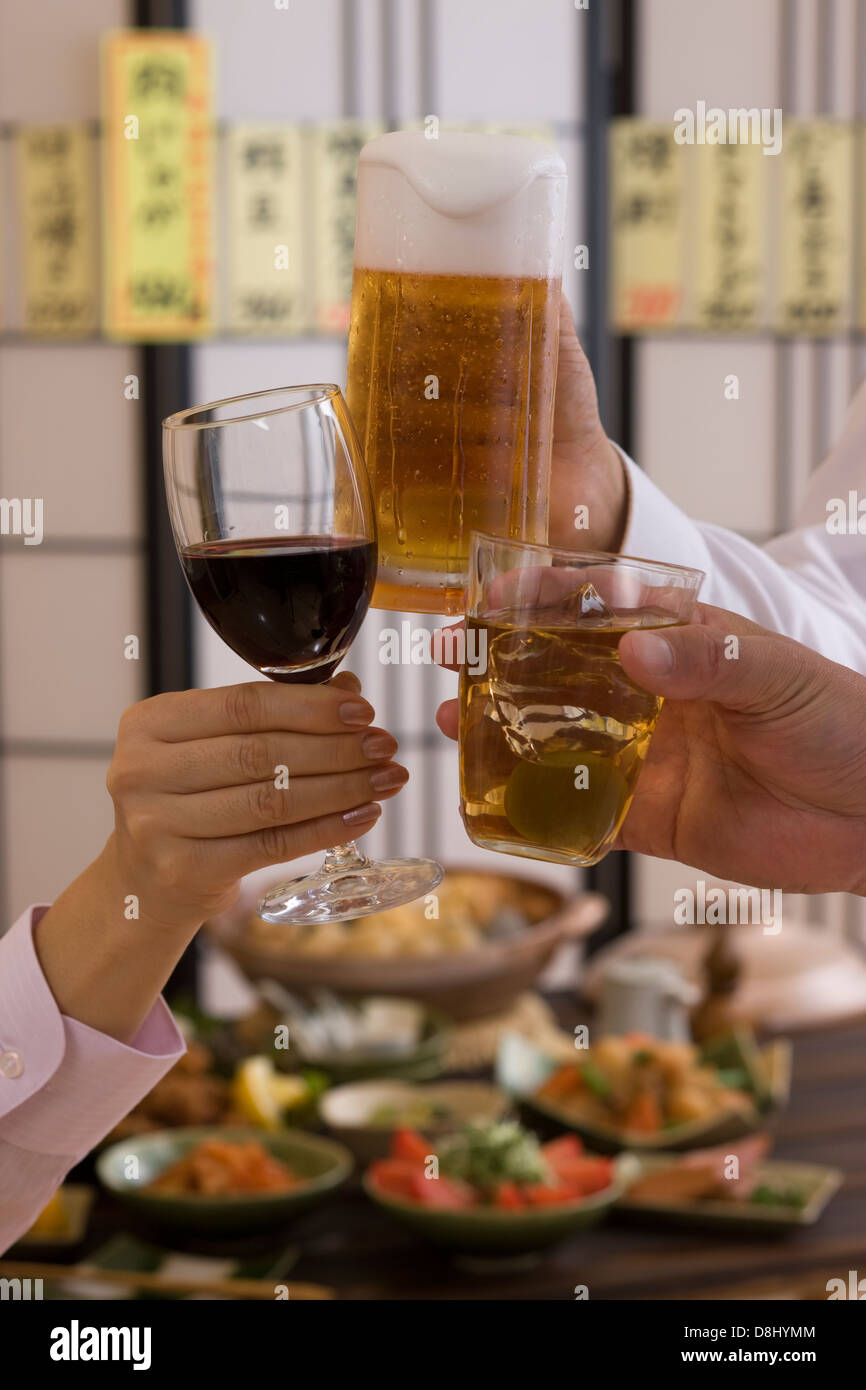 Drei Menschen, die miteinander mit verschiedenen Getränken in Izakaya Toasten Stockfoto