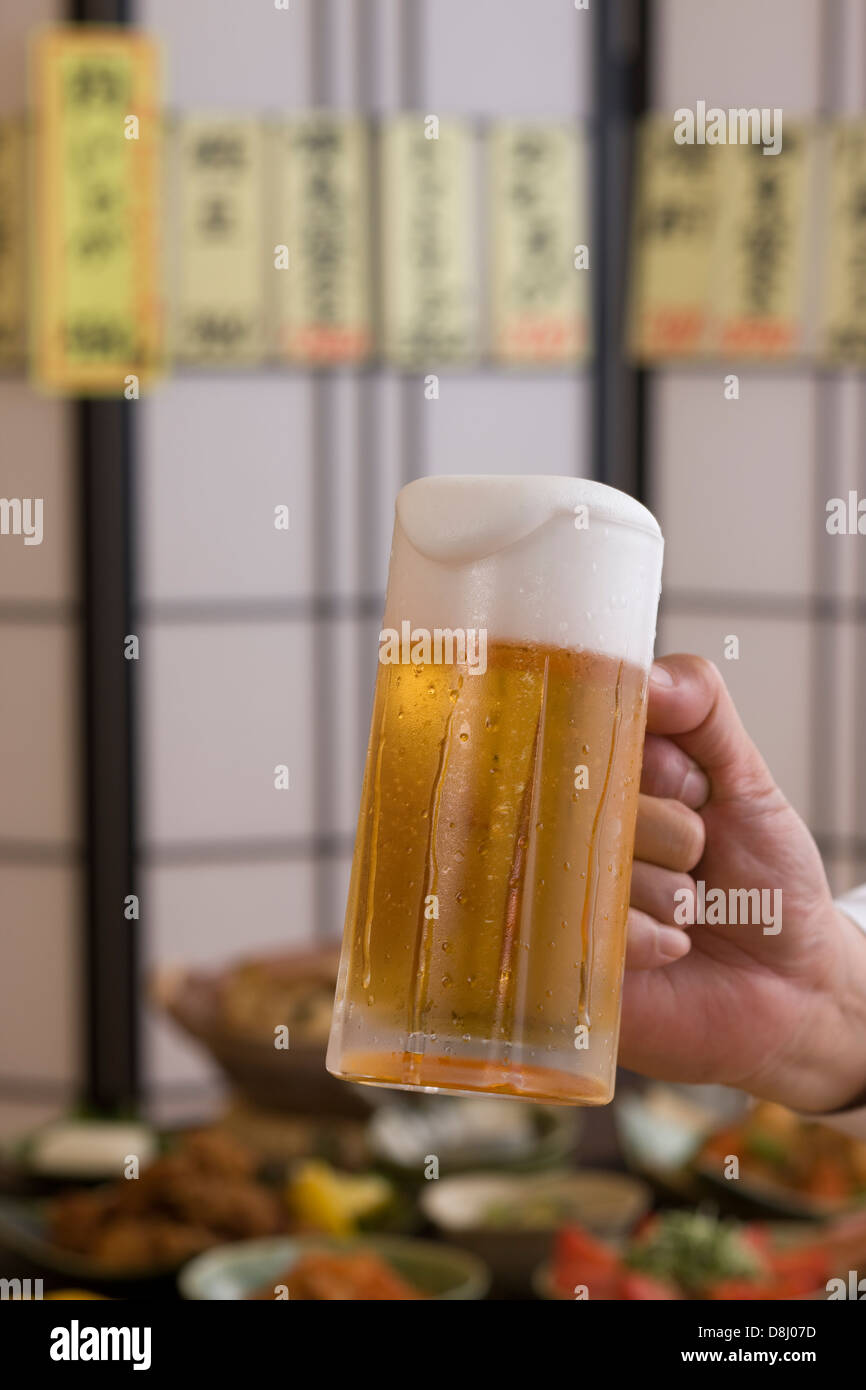 Menschliche Hand halten Krug Bier in Izakaya Stockfoto