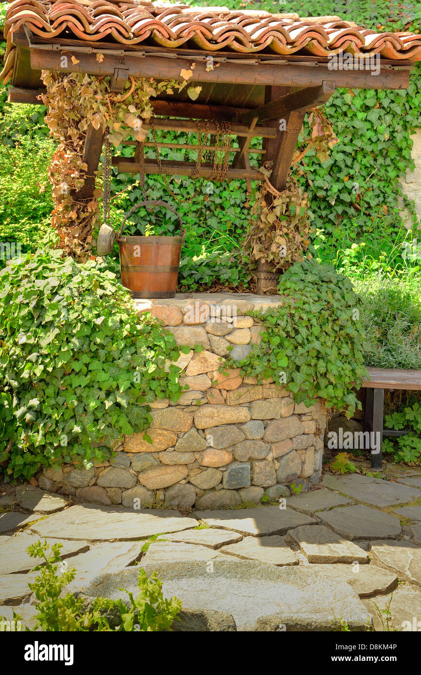 Alten Brunnen und ein hölzerner Eimer unter Efeu Blätter im Garten