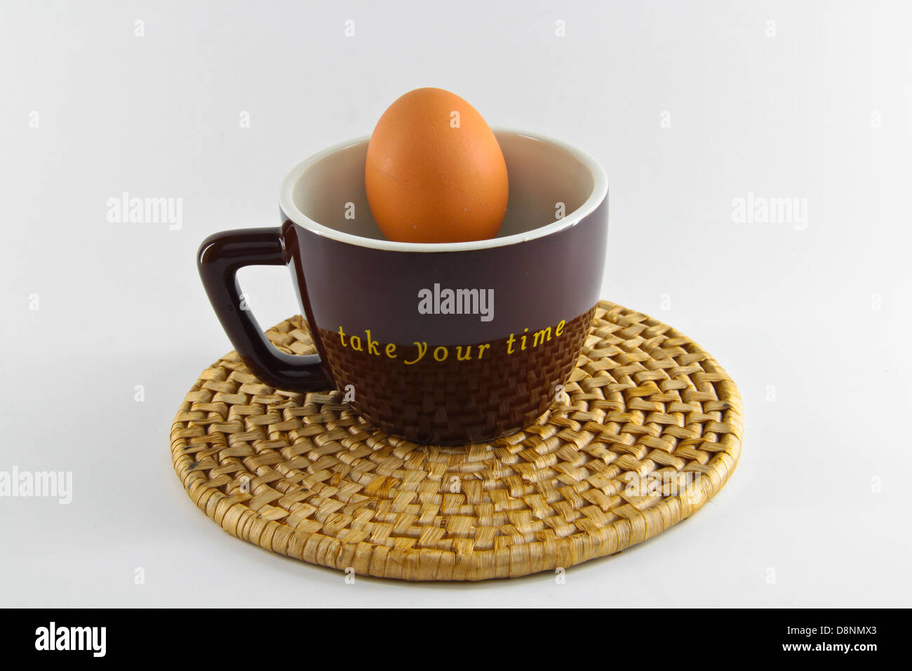 Braune Farbe Tasse mit rohem Ei und Formulierung nehmen Sie sich Zeit auf weiß. Konzept der Frühstück mit Ei und erfrischendes Getränk. Stockfoto