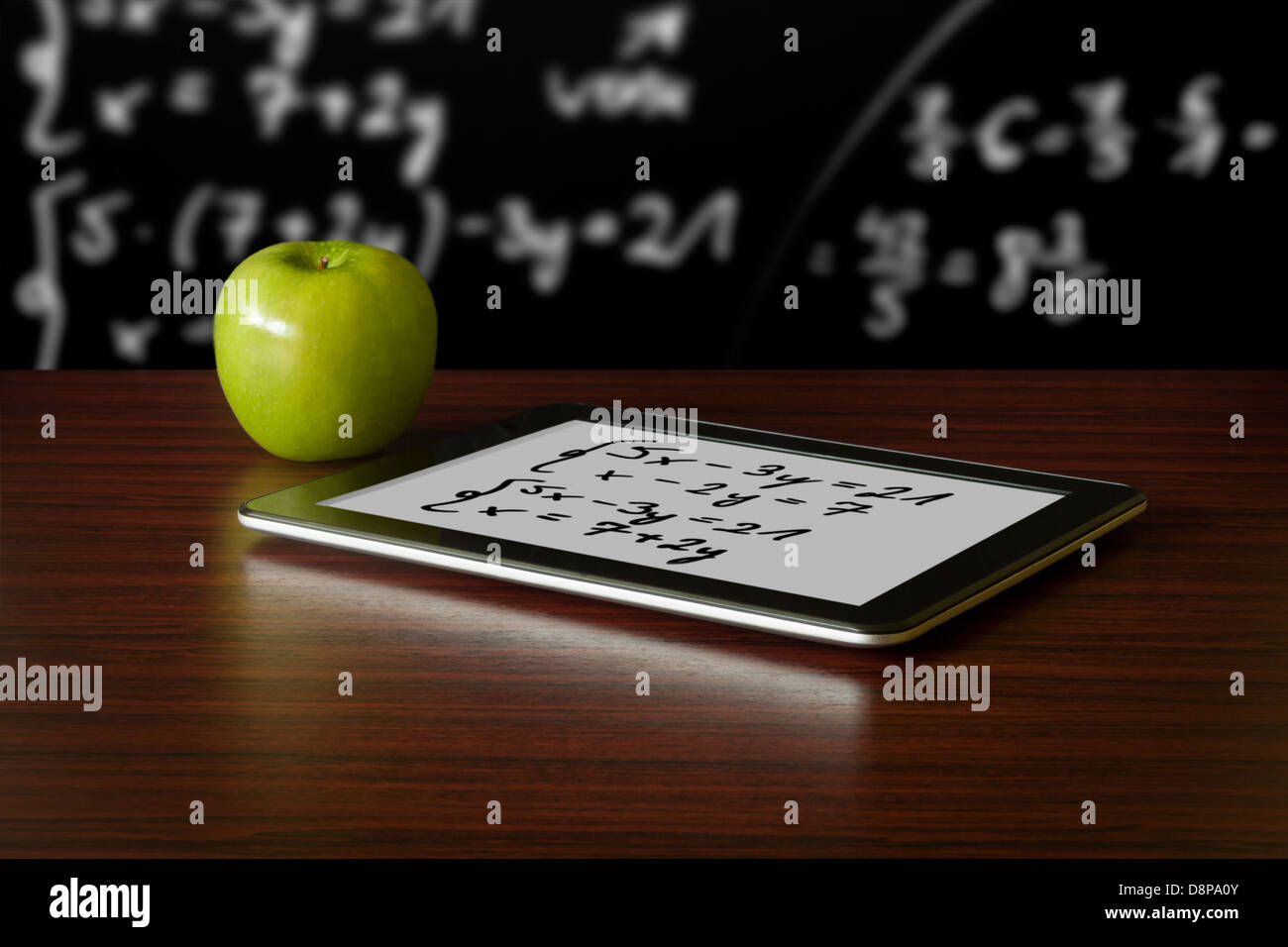Digital-Tablette und Apple auf dem Schreibtisch vor Tafel Stockfoto