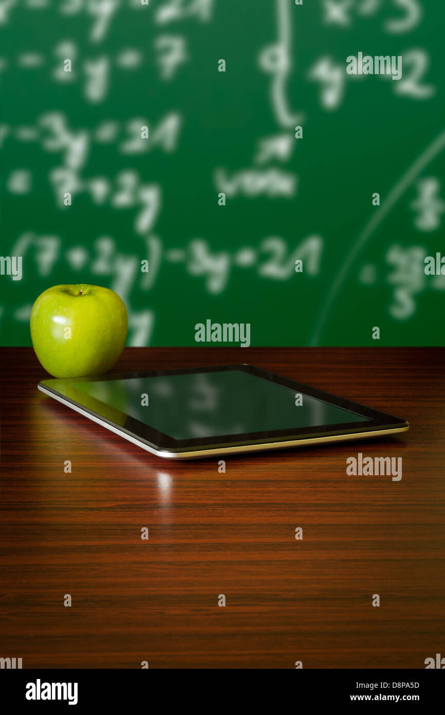 Digital-Tablette und Apple auf dem Schreibtisch vor Tafel Stockfoto