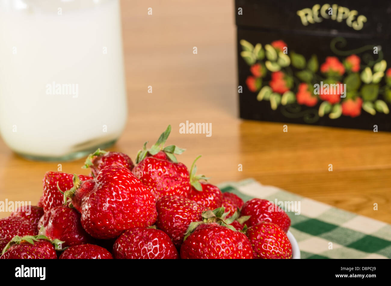 Eine Schale mit frischen Erdbeeren mit ein Rezept-Box und eine Milchflasche Stockfoto