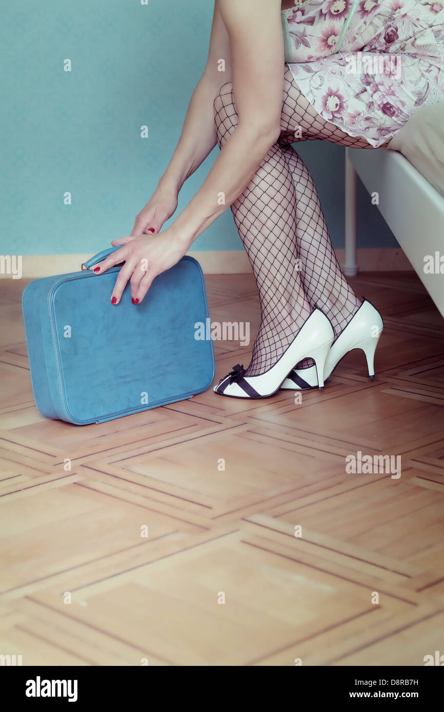 eine Frau in einem Negligé sitzt auf einem Bett mit einem Koffer Stockfoto