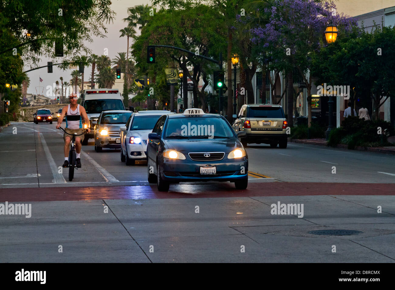 State Street in Santa Barbara, Kalifornien, die Autos mit Scheinwerfern auf Radfahrer und Fußgänger in der Abenddämmerung aufgenommen. Stockfoto