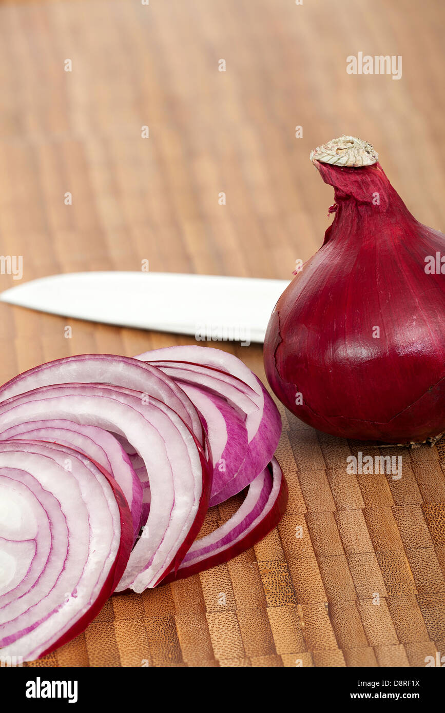 Eine ganze rote Zwiebel und Zwiebelringe mit einem Messer auf ein Schneidebrett Stockfoto