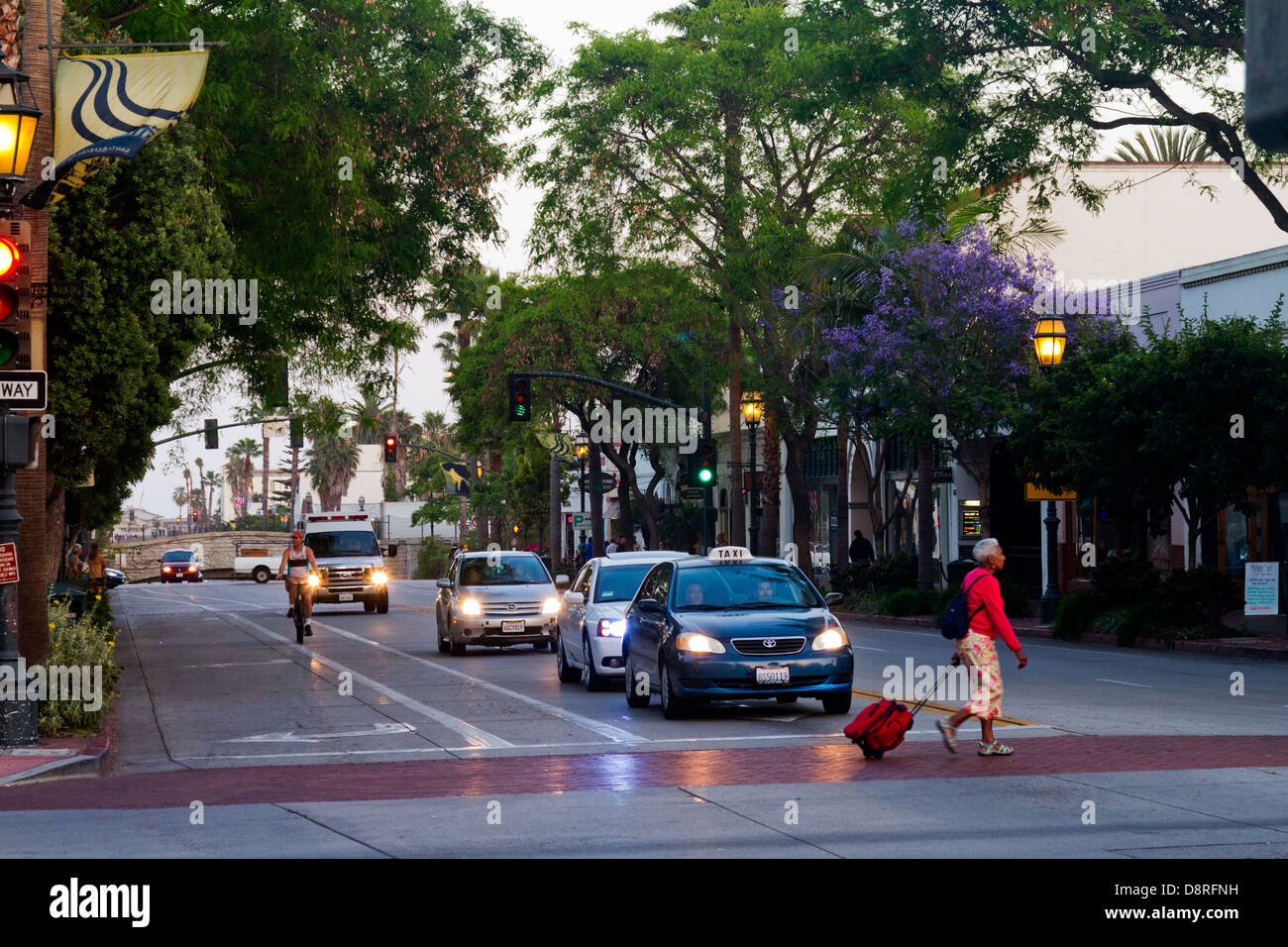 State Street in Santa Barbara, Kalifornien, die Autos mit Scheinwerfern auf Radfahrer und Fußgänger in der Abenddämmerung aufgenommen. Stockfoto