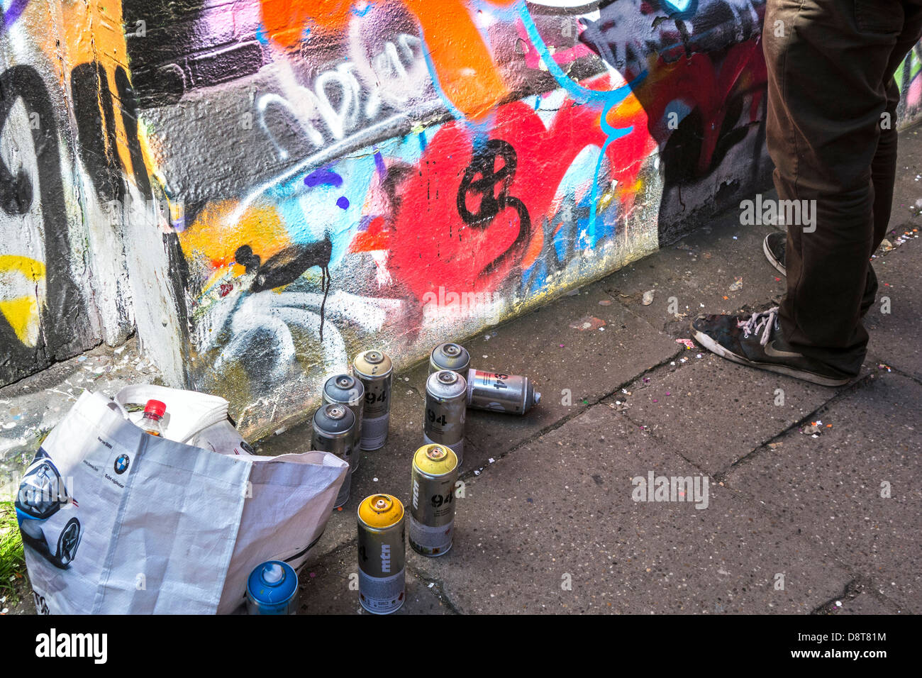 Spraydosen auf dem Boden und Youngster sprühen bunte Graffiti an der Wand des Gebäudes in der Stadt Stockfoto
