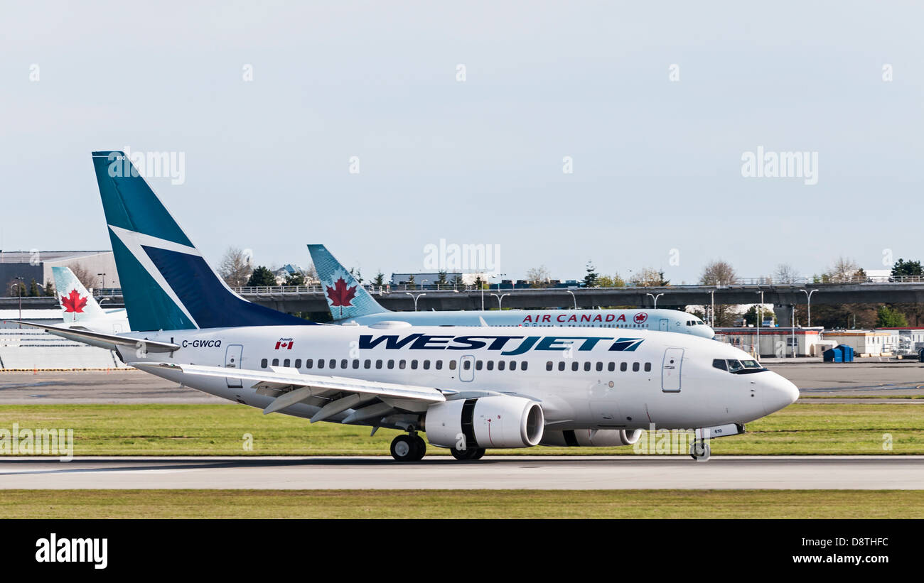 Eine Boeing 737-600 Westjet landet am Vancouver International Airport. Im Hintergrund sind zwei Air Canada Jetliner auf dem Rollfeld Stockfoto