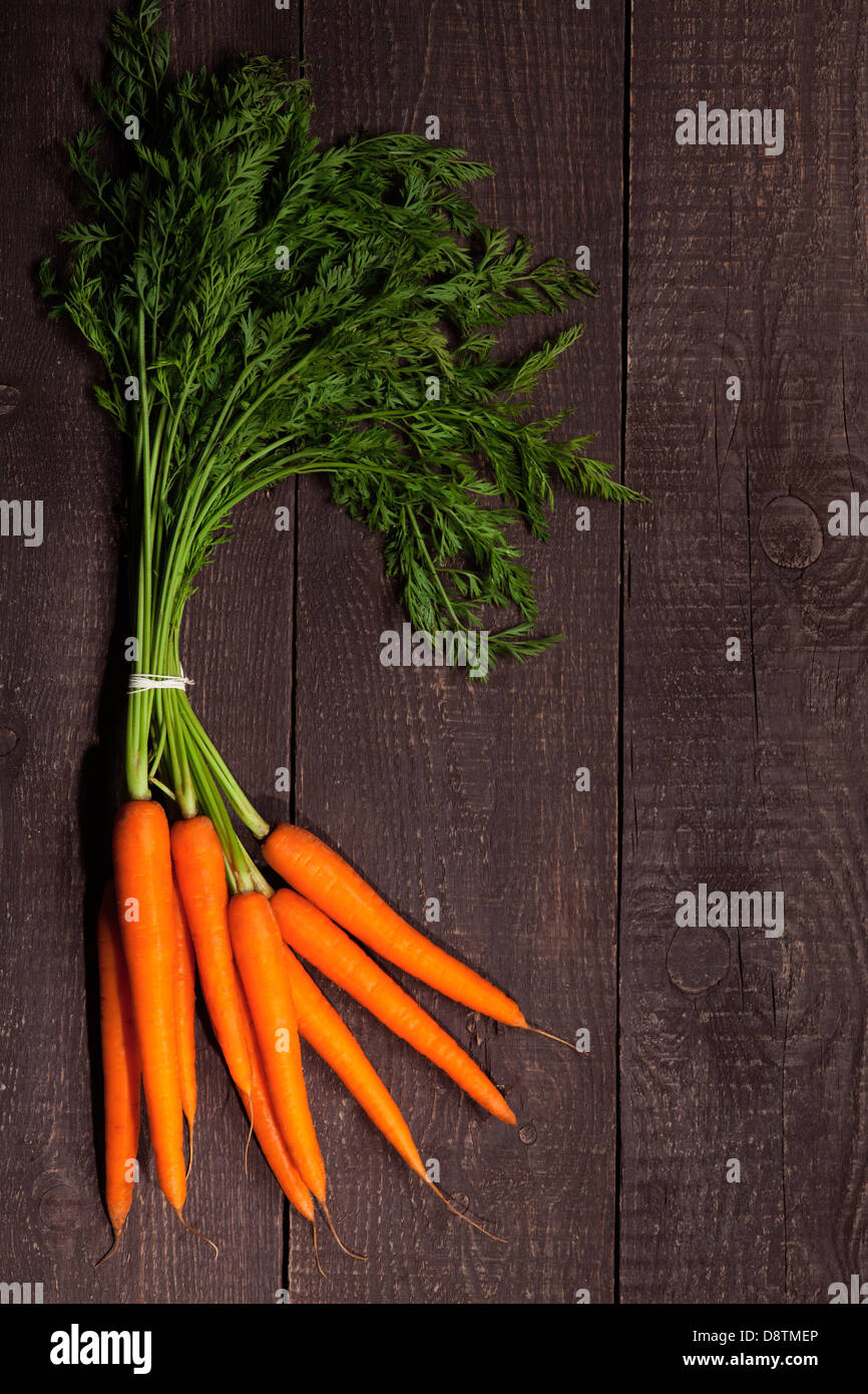 Reihe von Karotten mit Blättern auf braunem Holz Hintergrund Stockfoto