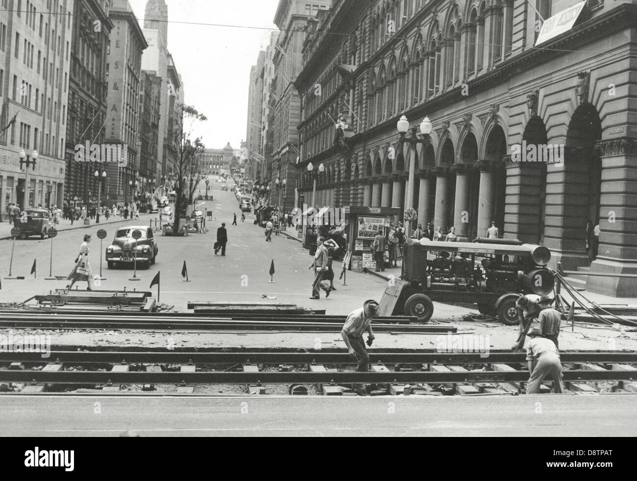 Dieses Schwarzweiß-Foto zeigt Straßenbahnschienen am Martin Place in Sydney mit historischen Elementen wie Oldtimern, einem Zeitungsstand und Arbeitern. Es fängt einen geschäftigen Moment in der Entwicklung der Stadt ein, mit einem klaren Blick auf das berühmte General Post Office von Sydney im Hintergrund. Stockfoto