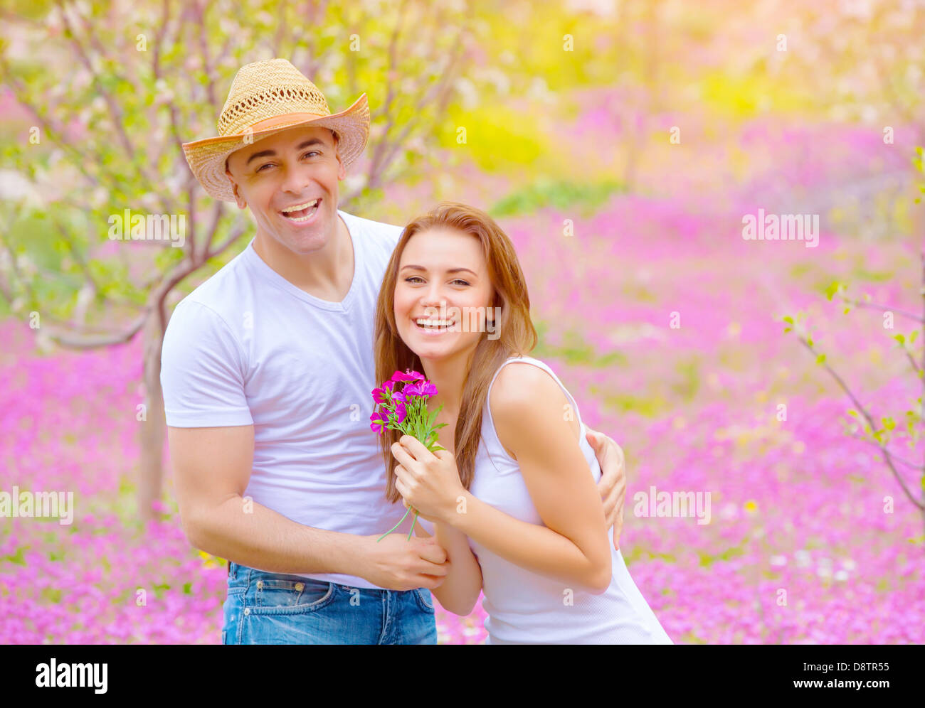 Glücklich lächelnde Paare, die Spaß im Sommerpark, Entspannung im Freien auf pink floral Lichtung, Romantik und Liebe Konzept Stockfoto