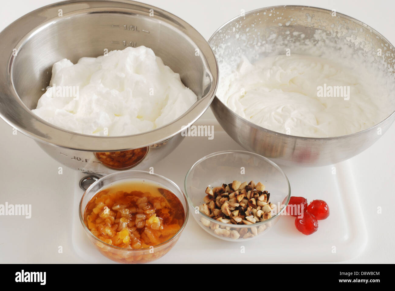 Schüssel mit Eischnee und eine Schüssel mit gepeitschter Creme, kleine Schüssel mit zerkleinerten getrockneten Früchten und Honig Stockfoto