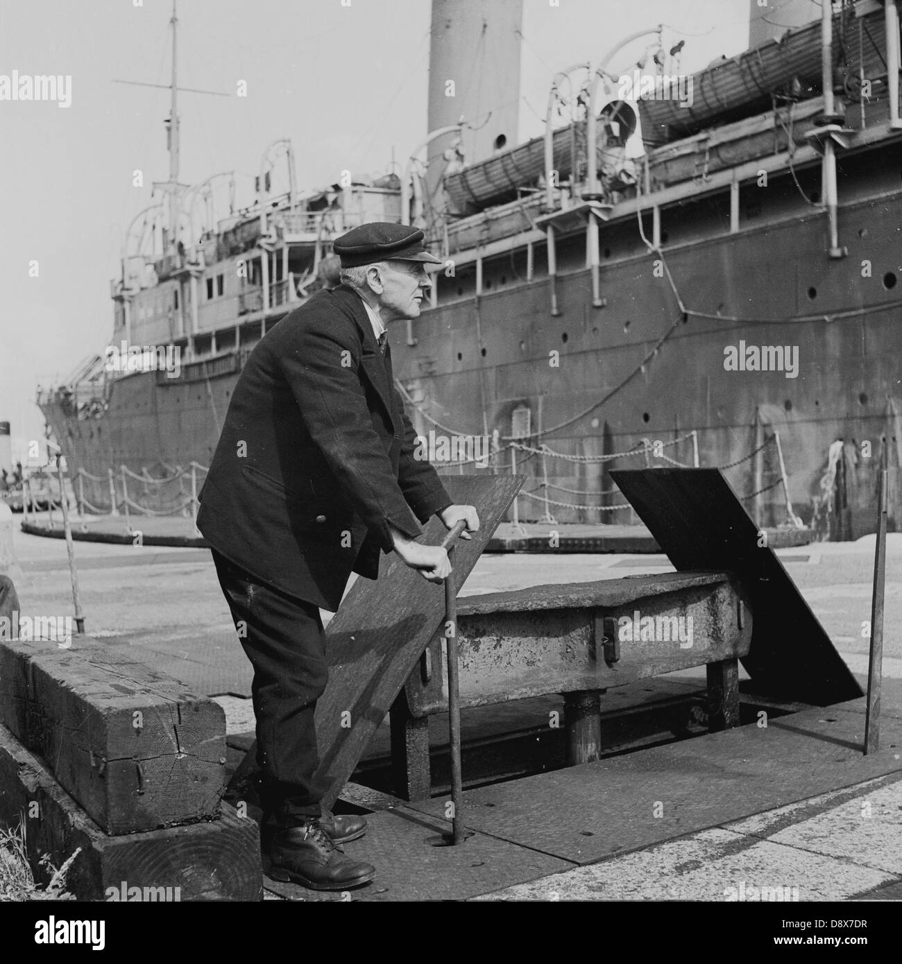 Historische der 1950er Jahre. Ein Versand-Operative oder Hafenarbeiter nutzt eine Winde um sicherzustellen, dass der Anker eines Schiffes richtig festgemacht ist. Stockfoto