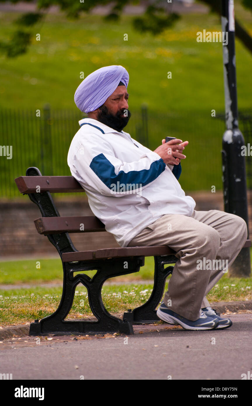 Sikh Mann sitzen draußen auf einer Bank mit Turban unten Stockfoto