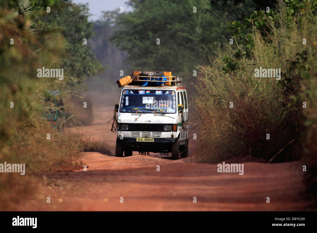 Gambia-Minibus fahren auf schmale, unbefestigte Straße bedeckt in roter Erde tragen Bestimmungen auf Dachträger Stockfoto