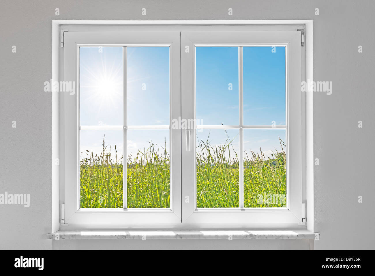 Bild einer weißen Wand mit weißen geschlossenen Fenster innen und außen grüne Wiese mit Sonne und blauer Himmel Stockfoto