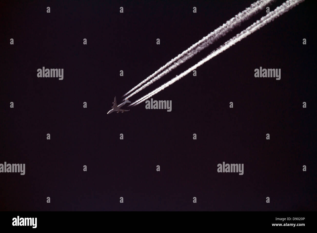 Düsenjet fliegt gegen einen schwarzen Himmel mit Kondensstreifen. Stockfoto