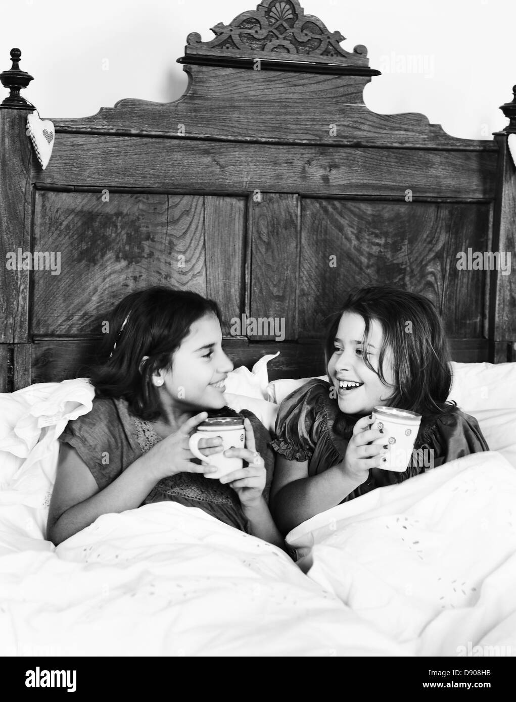 Zwei Mädchen mit einer Tasse heißer Schokolade in einem rustikalen Bett, Italien. Stockfoto