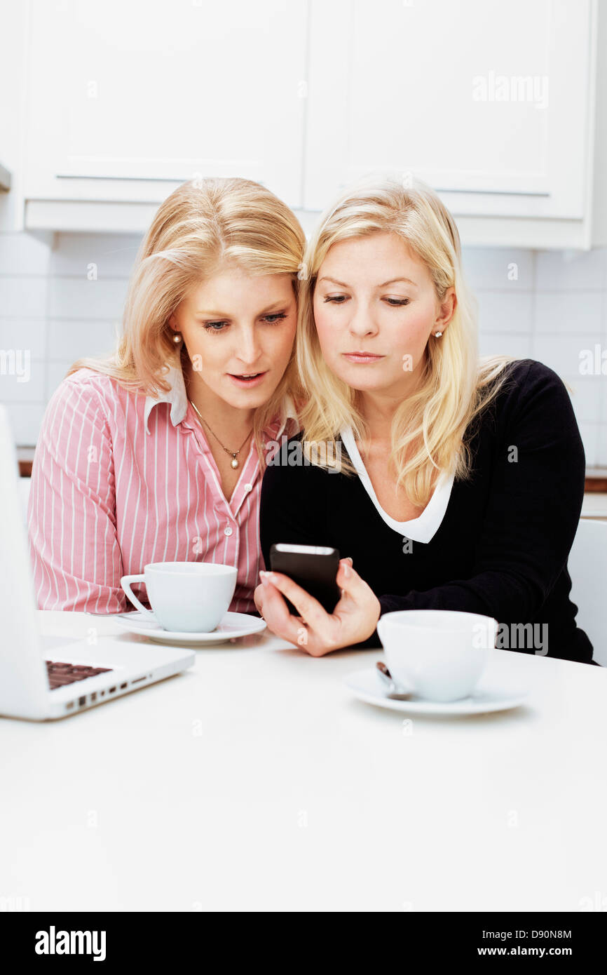 Zwei junge Frauen mit Handy in Küche Stockfoto
