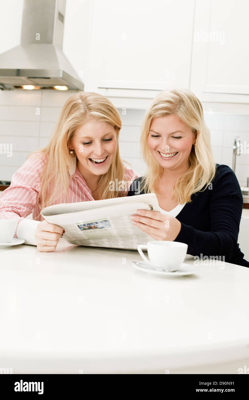 Zwei junge Frauen, die lesen Zeitung in Küche Stockfoto