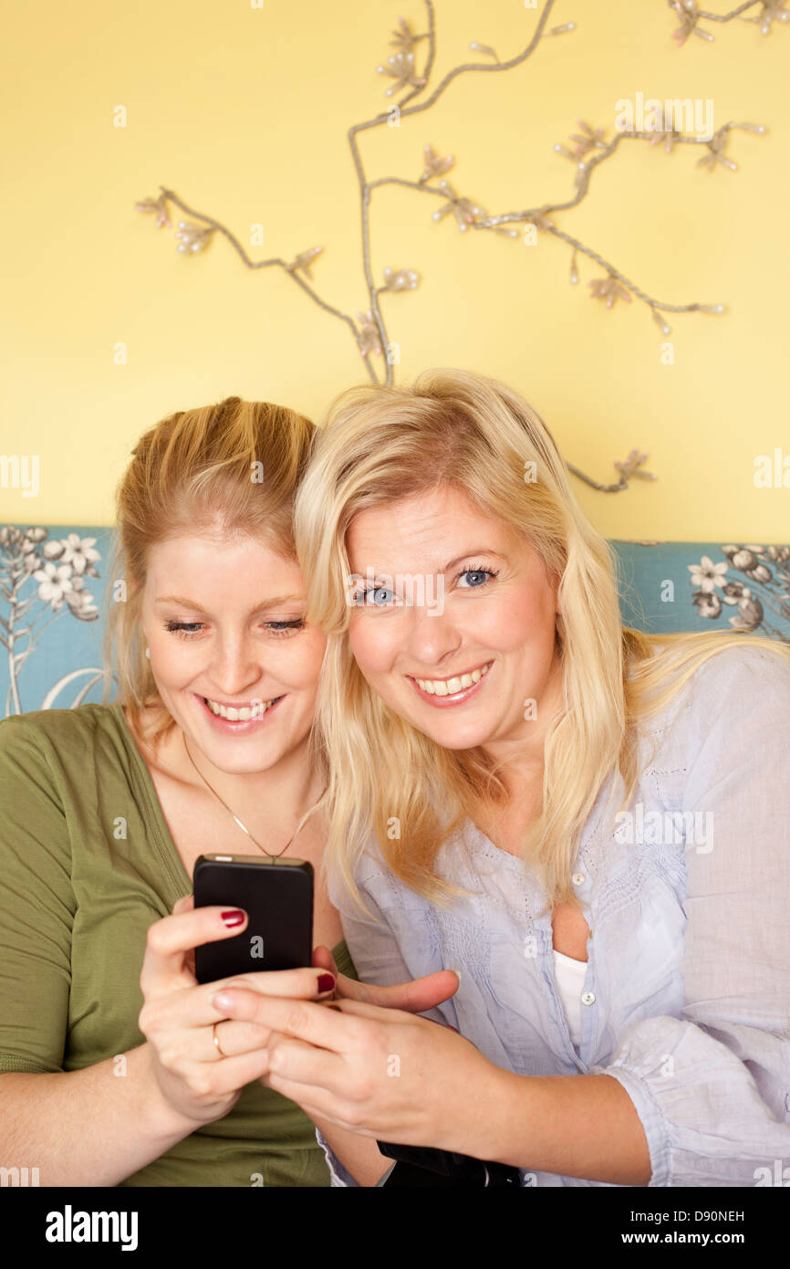 Zwei junge Frauen mit Handy im Schlafzimmer Stockfoto
