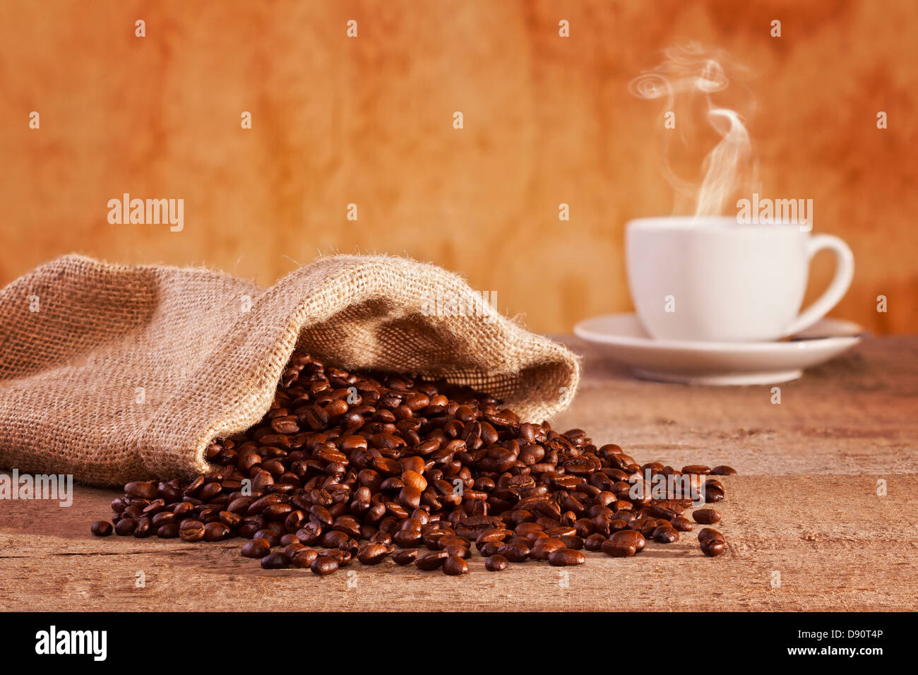 Kaffeebohnen und Leinensack - gerösteten Kaffeebohnen, die aus einem Leinensack, Tasse Kaffee mit sichtbaren Dampf verschütten... Stockfoto